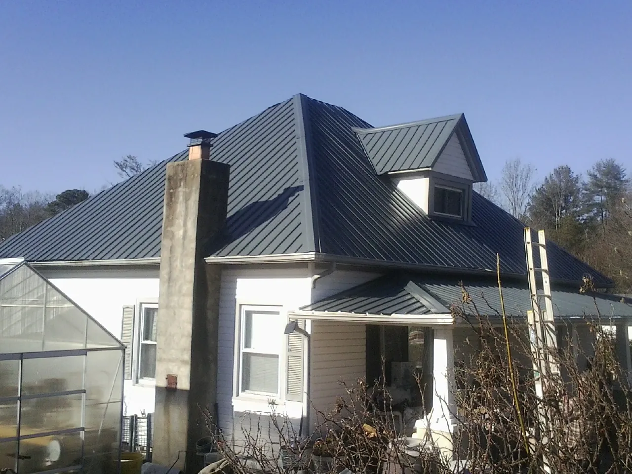 Dark blue standing seam metal roof on a white farmhouse with dormer — Slate & Tile Roof Repair by Roofing Brothers in Rosharon