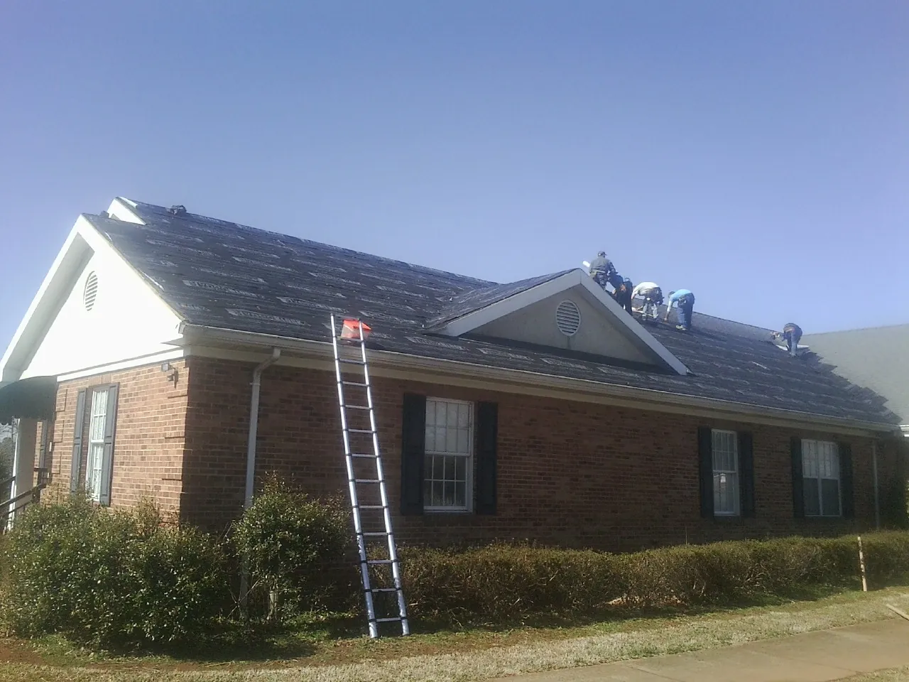 Crew tearing shingles off a brick ranch roof with a ladder set — Metal Roof Repair work by our crew in Rosharon