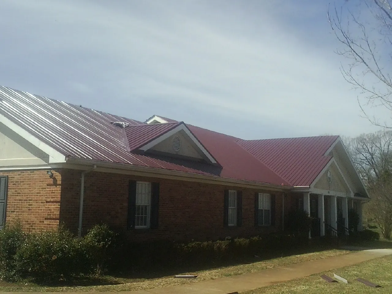 Red metal roof with gabled entries on a long brick building, from a Hail Damage Roof Repair job in Rosharon