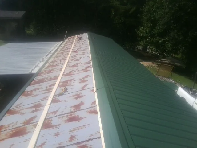 Old rusted panels beside newly installed green metal roofing — Wind Damage Roof Repair by Roofing Brothers in Rosharon