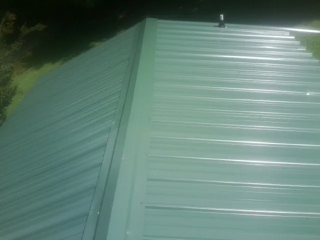 New green metal panels meeting at the ridge of a roof — Flat Roof Repair work by our crew in Rosharon