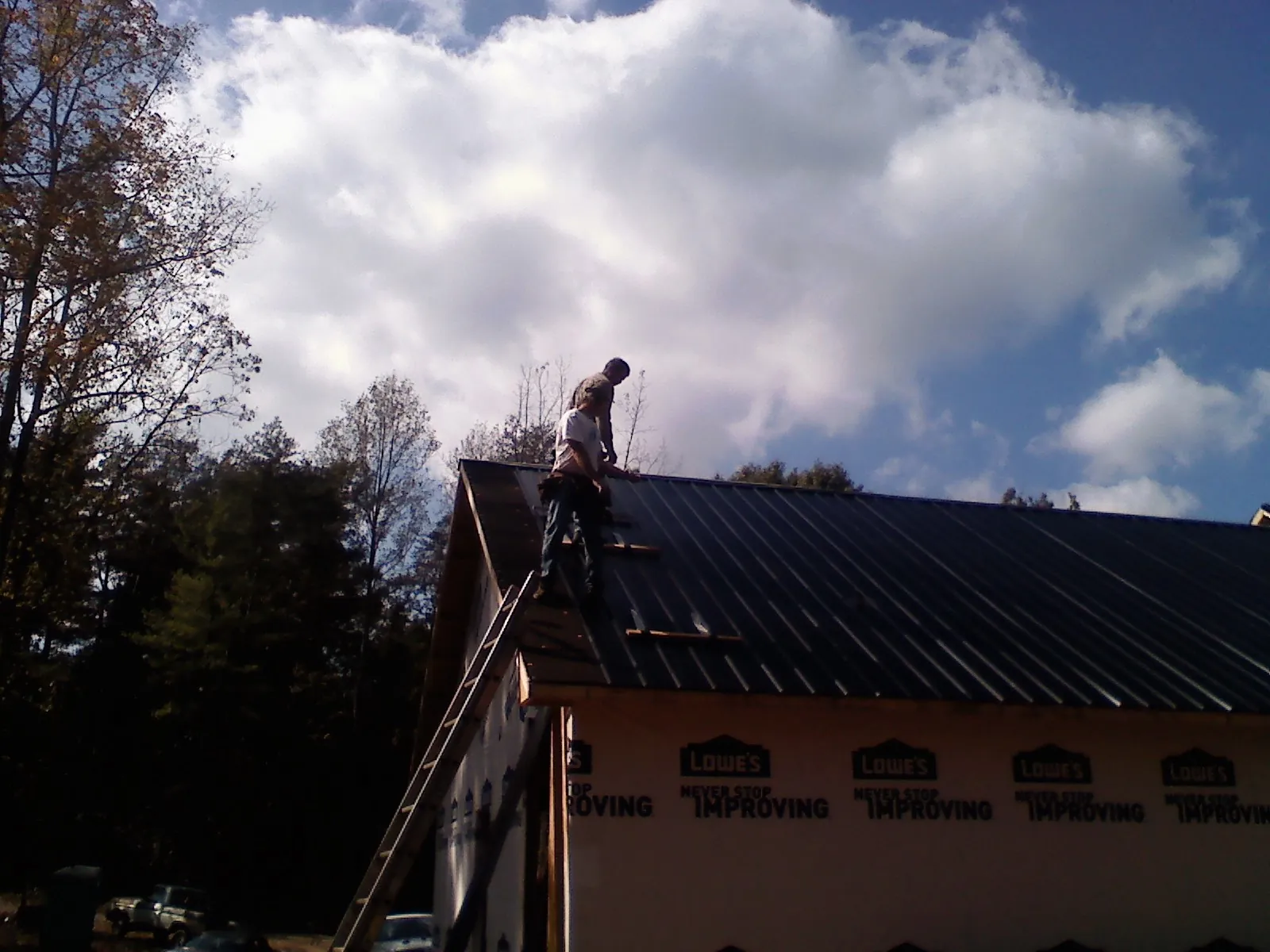 Roofer fastening dark metal panels high against a cloudy sky, from a Roof Inspection job in Rosharon