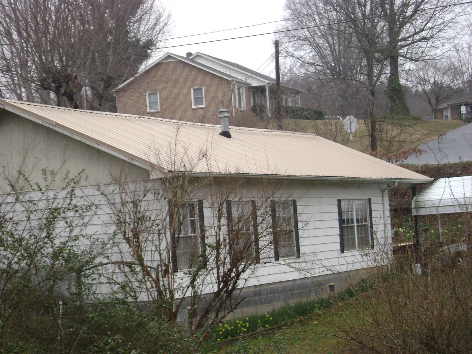 Tan metal roof on a white sided house set into a hillside — Commercial Roofing by Roofing Brothers in Rosharon